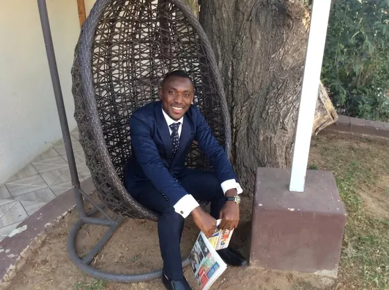 Valentine Golden Ghanem - Seated in a hanging wicker chair outdoors, navy suit, holding a magazine.