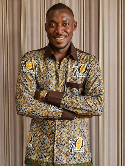 Valentine Golden Ghanem - Portrait, arms crossed, Ghana COCOBOD 70th Anniversary patterned shirt.