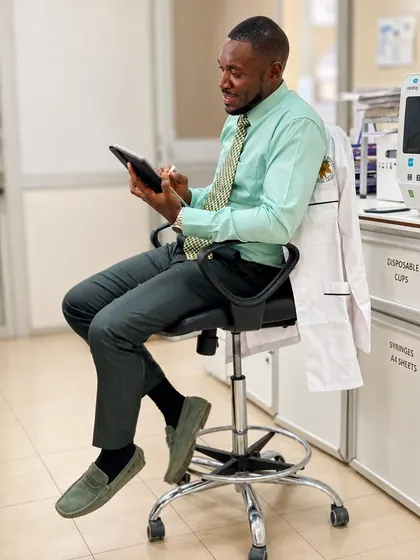 Valentine Golden Ghanem - On a lab stool, mint-green shirt, reviewing a tablet, coat draped behind him.