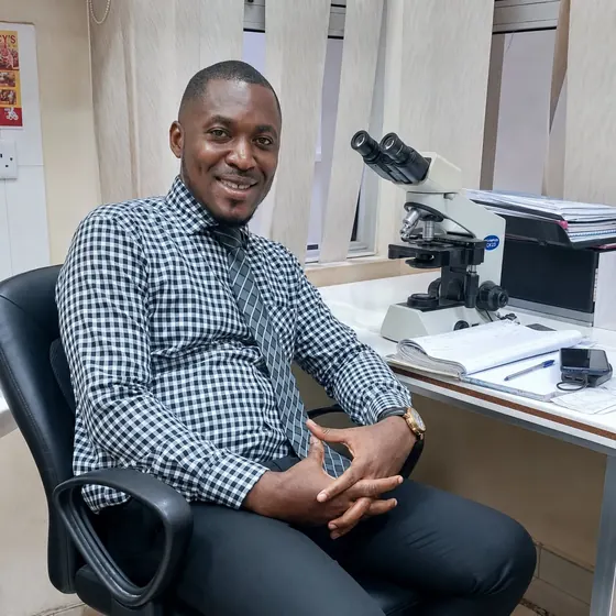 Valentine Golden Ghanem - At the laboratory desk, checkered shirt, beside the microscope.